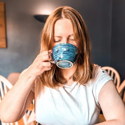 Profile photo of Wendy England, CEO and founder of Her Cozy Gaming. White woman drinking from a blue teacup.